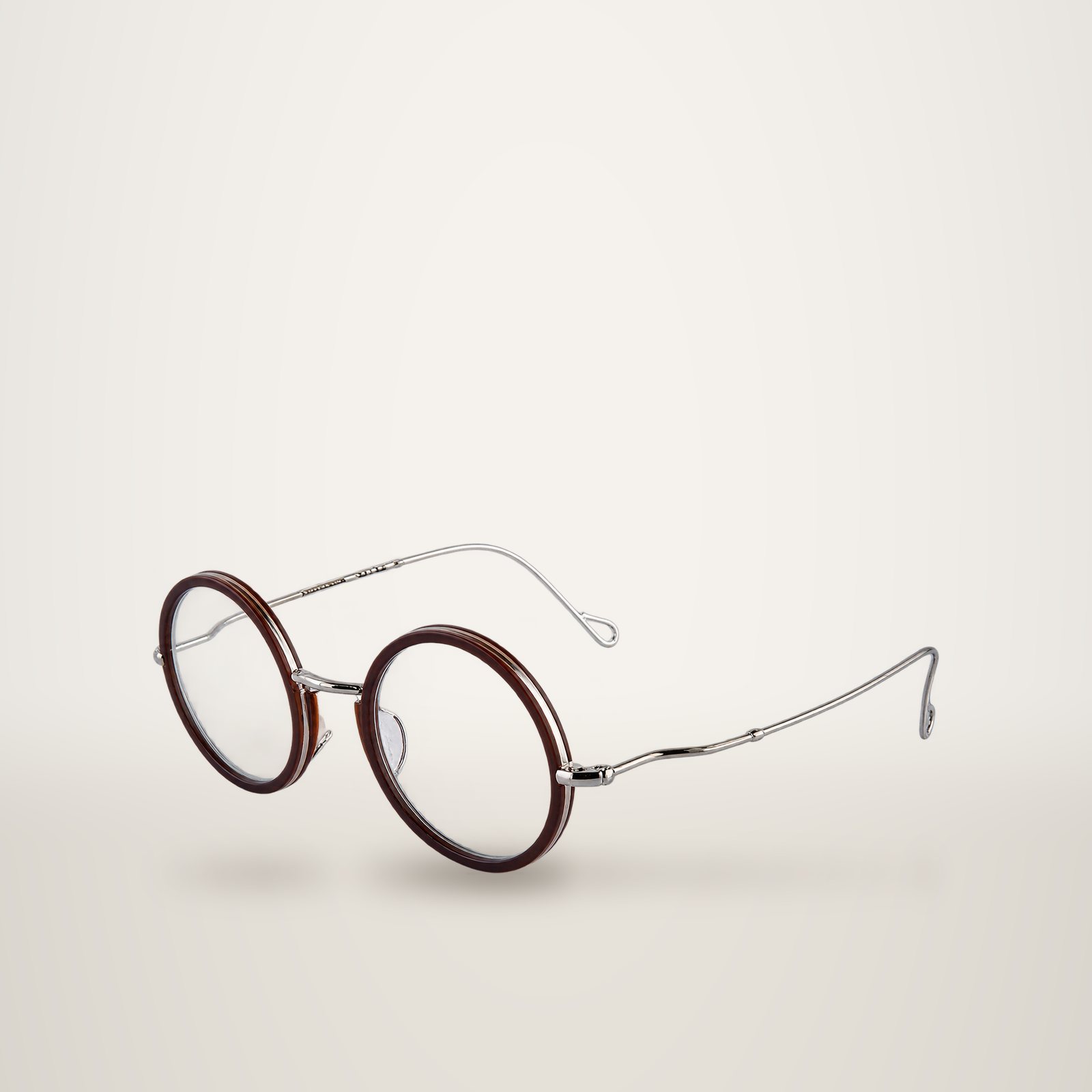 Paire de lunettes rondes à monture marron foncé et fines branches argentées, posée sur un fond blanc uni.