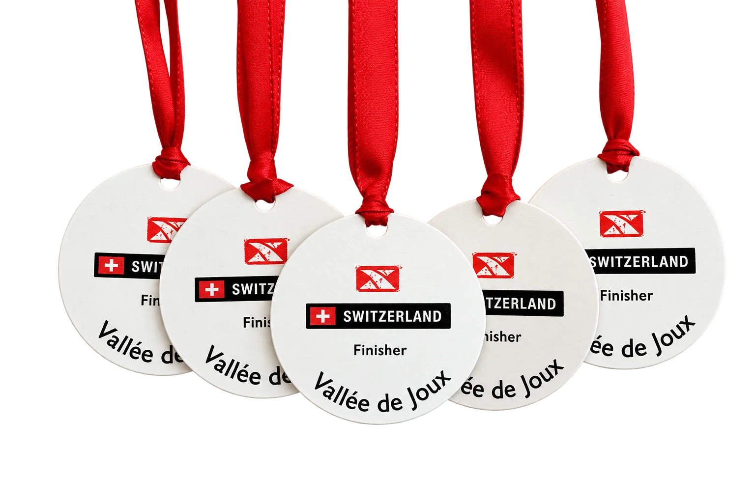 Cinq médailles rondes blanches suspendues à des rubans rouges, portant les mentions Switzerland, Finisher et Vallée de Joux, posées sur un tissu clair.